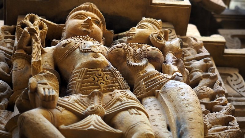 Intricately carved sandstone sculpture of a celestial couple adorned with elaborate jewelry and garments on the walls of an ancient Jain Temples in Jaisalmer, Rajasthan, India, showcasing exquisite craftsmanship and detailed artistry