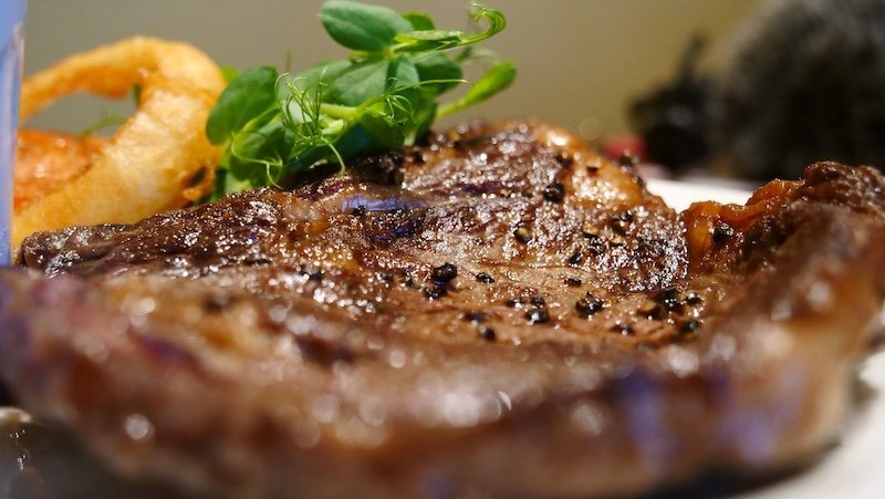 Juicy peppercorn-seasoned steak served during a Ireland road trip, garnished with fresh pea shoots and paired with crispy onion rings — showcasing the hearty and flavorful cuisine travelers can enjoy across Ireland