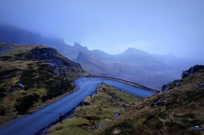 A winding road through the foggy landscapes of the Isle of Skye in Scotland, surrounded by rocky cliffs, rolling moors, and mist-covered peaks, capturing the dramatic and mysterious beauty of this iconic Scottish Highlands destination