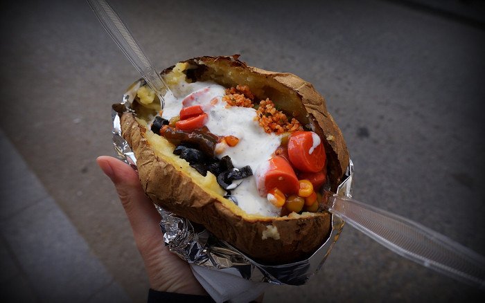 Close-up of a freshly baked Kumpir in Istanbul, Turkey, overflowing with toppings like sweetcorn, cherry tomatoes, olives, yogurt sauce, and crispy bits