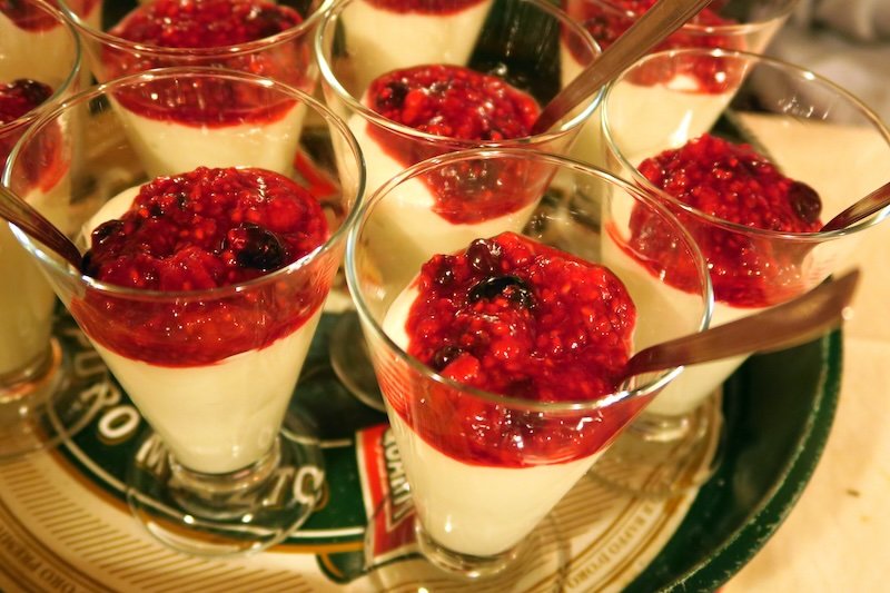 Glasses of creamy Italian dessert topped with fresh berry compote, served with spoons on a tray in Emilia-Romagna, Italy, showcasing the region’s culinary creativity and sweet traditions that make it a must-visit destination for food lovers