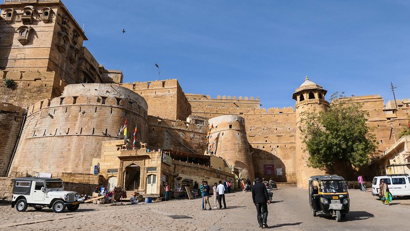 Visitors walk and ride tuk-tuks past the towering yellow sandstone walls of Jaisalmer Fort in Jaisalmer, India, a historic desert citadel that dominates the old city skyline