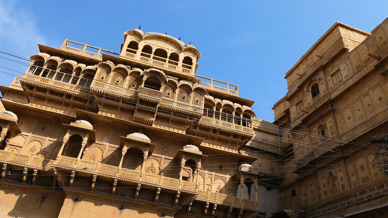 Ornately carved golden sandstone façade of a historic haveli in Jaisalmer, India, showcasing intricate balconies, arched windows, and latticework typical of the city’s royal merchant mansions