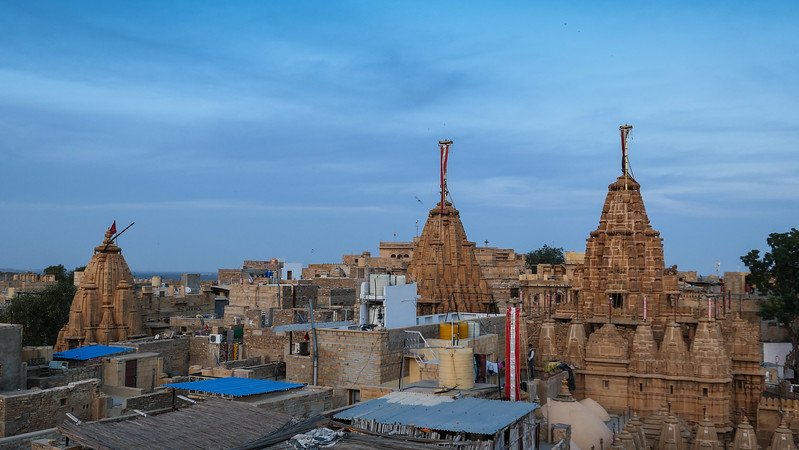Panoramic view of the intricately carved Jain Temples rising above the golden sandstone rooftops of Jaisalmer, India, glowing under a serene evening sky in the heart of the Thar Desert