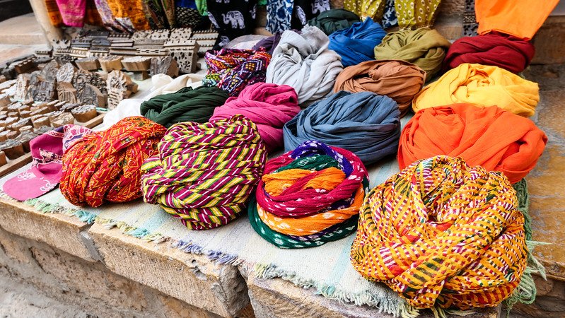 Vibrant display of traditional Rajasthani turbans and scarves in Jaisalmer, India, featuring bright colors and intricate patterns laid out at a local market stall