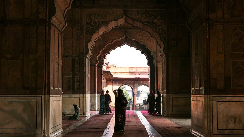 Interior of Jama Masjid prayer hall in Delhi, India, featuring Mughal arches, marble inlay, and worshippers in traditional dress