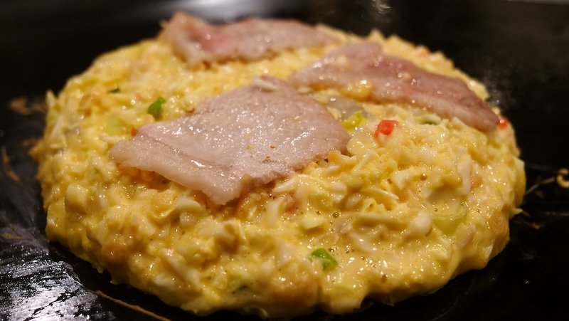 Japanese okinomiyaki osaka-style being cooked raw in front of our eyes in Osaka, Japan 