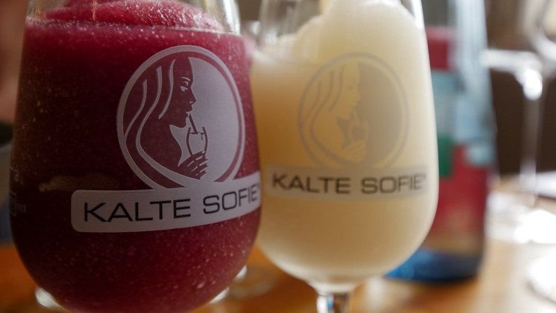 Close-up of two refreshing Kalte Sophie wine slushies—one red and one white—served in branded glasses at Alte Wache wine bar in Freiburg im Breisgau, Germany during summer