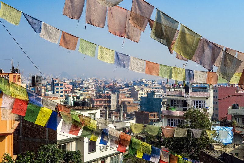 Colorful Buddhist prayer flags fluttering above the rooftops of Kathmandu, Nepal, with panoramic views of the bustling city below