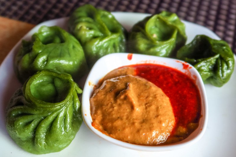 Plate of vibrant green spinach momos served with spicy red chili sauce and creamy sesame dip at a local eatery in Kathmandu, Nepal