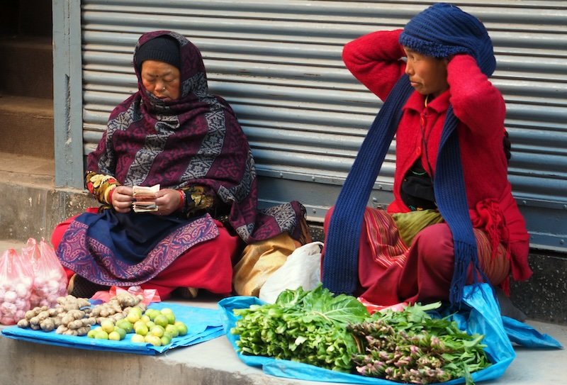 Local women vendors in Kathmandu selling fresh vegetables and counting cash at a traditional street market in Nepal.