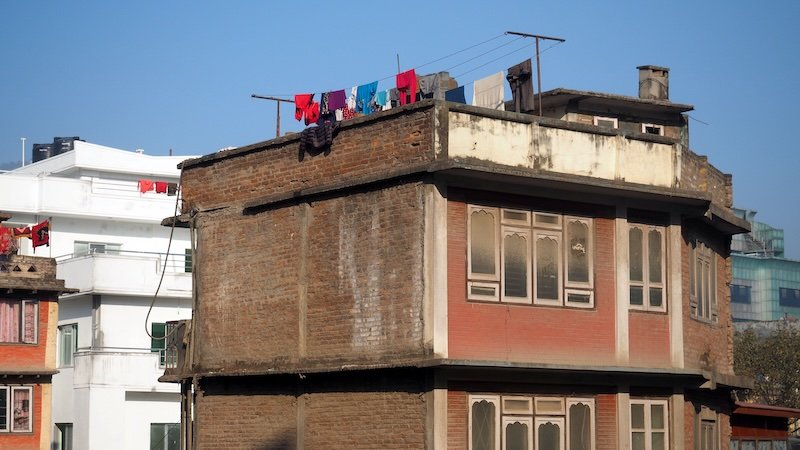 Traditional brick house in Kathmandu, Nepal, with colorful laundry drying on the rooftop, showcasing everyday local life and urban culture in the city.