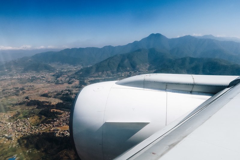 View of Kathmandu Valley and Himalayan foothills from airplane window while flying into Nepal, showcasing dramatic mountain scenery