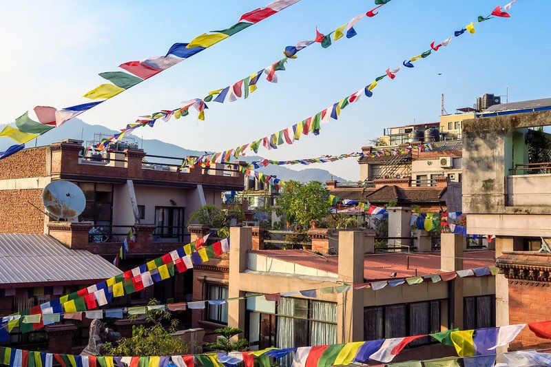 Colorful Buddhist prayer flags strung across rooftops with mountain views in Kathmandu, Nepal