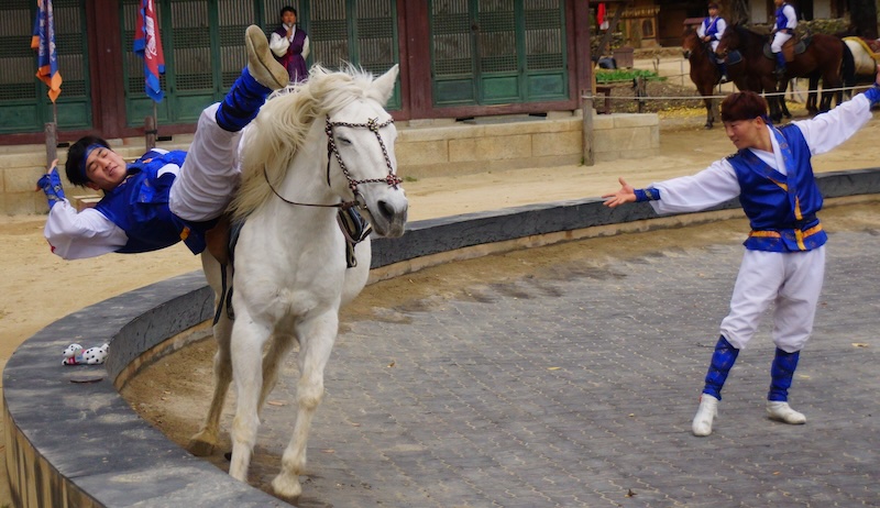 Korean equestrian performer reaching down from the horse to grab an item at the Korean Folk Village 