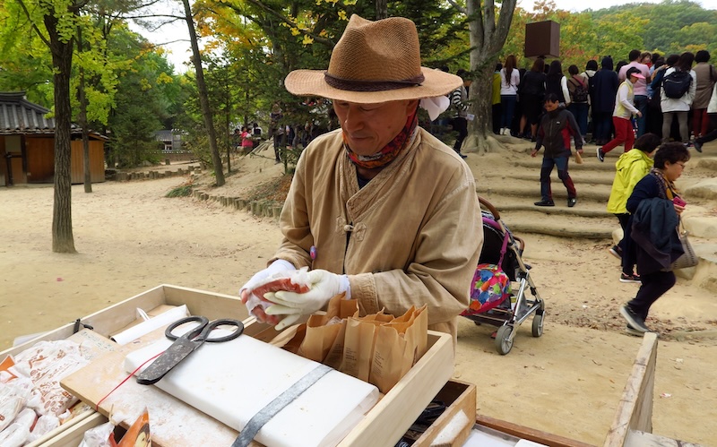 Korean man in traditional clothes cutting pumpkin taffy at the Korean Folk Village in Yongin, South Korea 