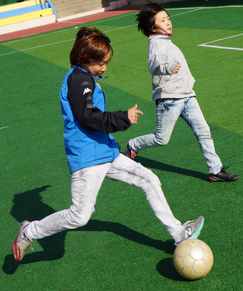 Korean students playing soccer outside at the field in South Korea 