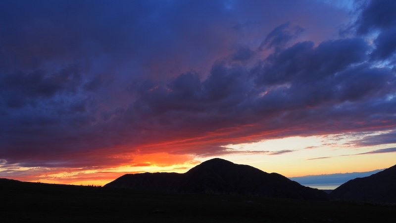 Dramatic sunset over the mountains in Kyrgyzstan with vibrant orange, pink, and purple clouds silhouetting the dark ridgelines during the 3-Day Panorama Trek