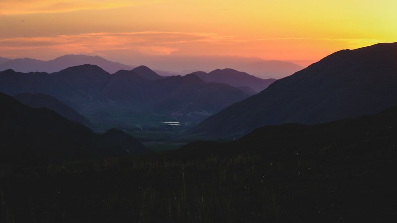 Golden sunset casting warm light over layers of dark mountain silhouettes and valleys on the final evening of the 3-Day Panorama Trek in Kyrgyzstan