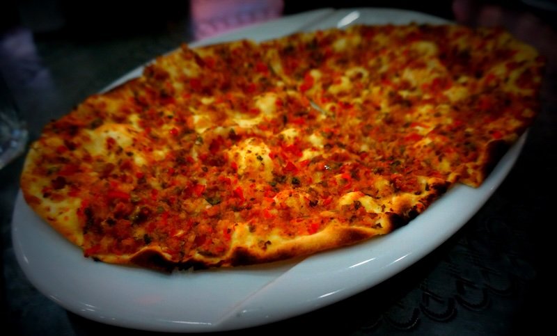 Close-up of freshly baked Lahmacun, a thin Turkish flatbread topped with minced meat, tomatoes, onions, and herbs, served hot on a white plate at a local eatery in Istanbul, Turkey