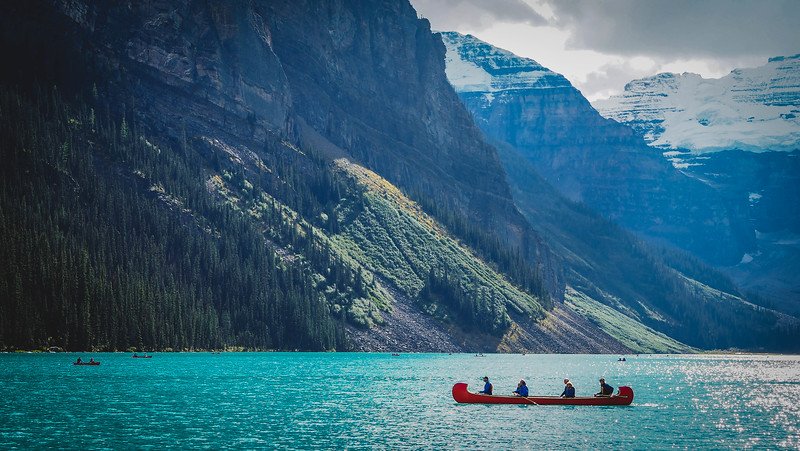 A red canoe gliding across the brilliant turquoise waters of Lake Louise, surrounded by steep forested mountain slopes and distant glaciers in the Rocky Mountains during our Canadian Rockies road trip