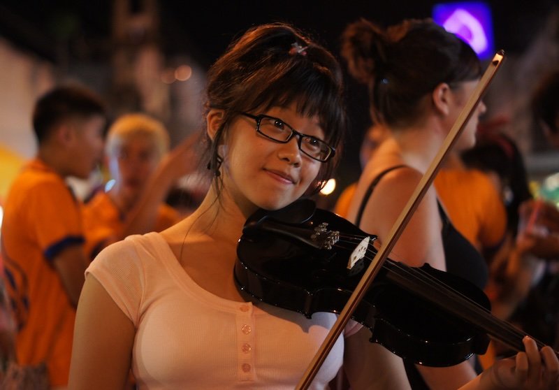 Local Thai girl playing violin to entertain the crowds at the Saturday Night Market in Chiang Mai, Thailand 