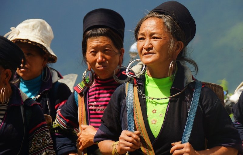 Local women in traditional embroidered attire and silver jewelry walking together during a cultural encounter along a trekking route in Sapa, Vietnam