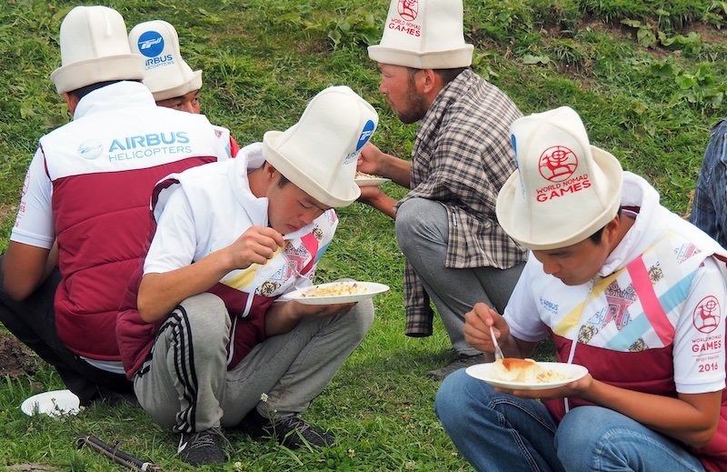 Locals eating food at the World Nomad Games in Kyrgyzstan squatting down for a bite to eat 