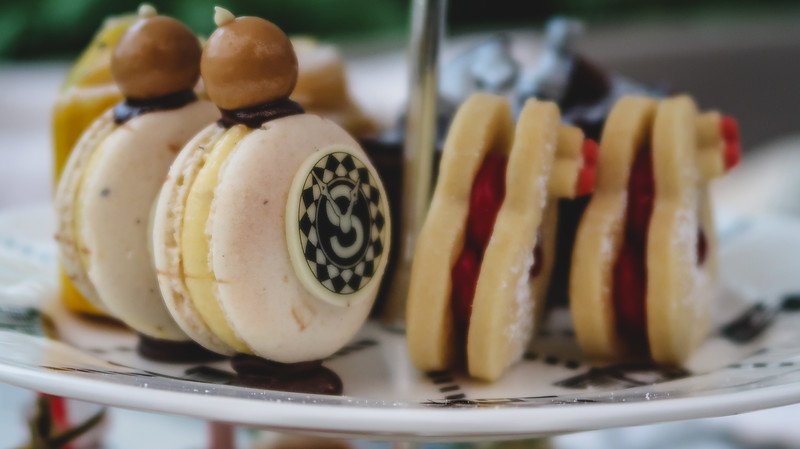 Close-up of whimsical desserts from Mad Hatter’s Afternoon Tea in London, including macarons topped with hazelnuts and cookies filled with jam, presented on a tiered stand and inspired by the playful Alice in Wonderland theme