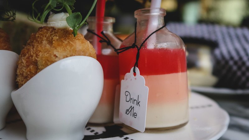 Close-up of the whimsical “Drink Me” potion served at Mad Hatter’s Afternoon Tea in London, presented in a small glass bottle with layered colors, paired with savory bites, evoking the playful Alice in Wonderland-inspired dining experience