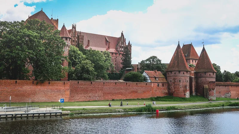 Malbork Castle as seen from the backside on the Nogat River with pedestrians and folks riding bicycle enjoying relaxation and leisure in Poland