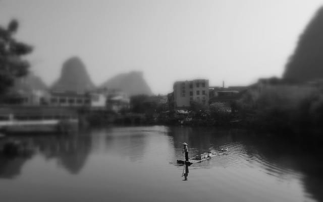 Man on a bamboo raft out on the water in Yangshuo, Guangxi, China with select focus