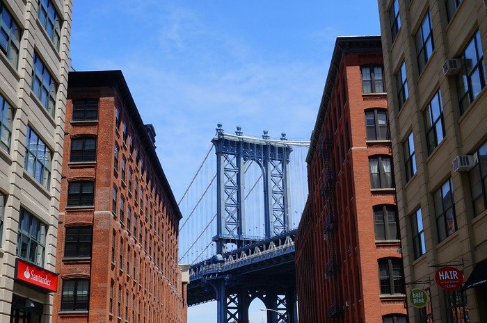 The Manhattan Bridge framed perfectly between two red-brick warehouse buildings in the DUMBO neighborhood of Brooklyn, New York City. This iconic viewpoint, located Down Under the Manhattan Bridge Overpass, is a popular photography and sightseeing spot