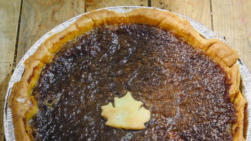Traditional maple syrup pie topped with a decorative maple leaf pastry, photographed on a rustic wooden table in Sutton, Quebec’s Eastern Townships during a local food tasting