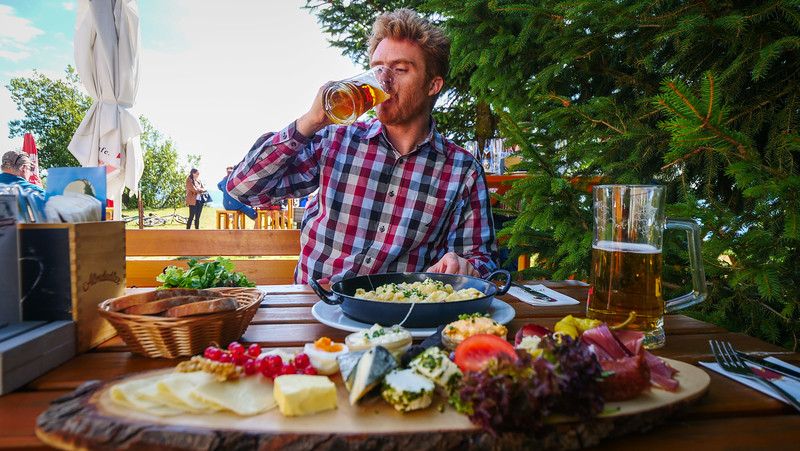 Marend is an Austrian snack that features a mix of mountain cheeses, cured meats, sausages, bread, and more with Nomadic Samuel enjoying a pint of beer