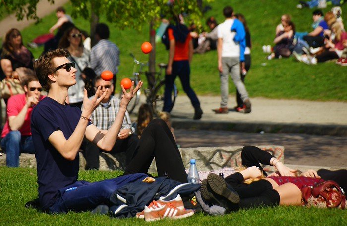 Mauerpark in Berlin, Germany on a Sunday afternoon with people relaxing on the grass, a man juggling orange balls, and groups socializing in the background, capturing the park’s lively atmosphere and creative community spirit
