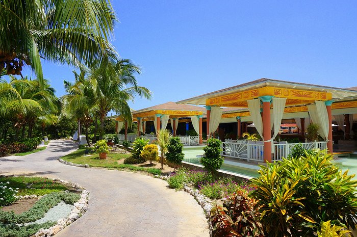 Tropical gardens and palm trees surround colourful open-air pavilions draped with flowing curtains under a brilliant blue sky at Melia Las Dunas resort in Cayo Santa María, Cuba, creating a vibrant and relaxing honeymoon atmosphere
