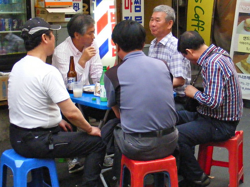 Men enjoying Food and Beer in Seoul, South Korea gathered on plastic chairs and a plastic table enjoying socializing