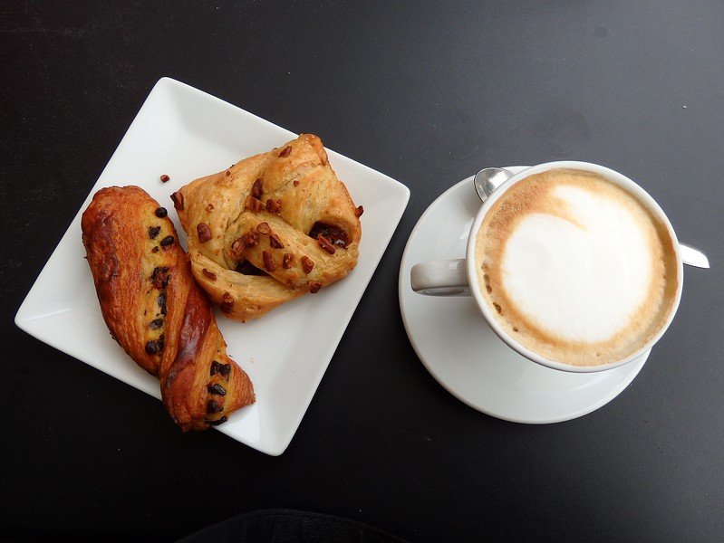 Freshly baked Italian pastries served on a square white plate alongside a frothy cappuccino, capturing a classic breakfast experience in Milan, Italy