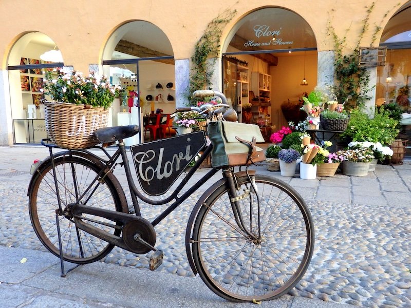 Charming vintage bicycle with a flower-filled basket parked outside a boutique flower shop in Milan, Italy, adding to the city’s stylish and romantic street atmosphere