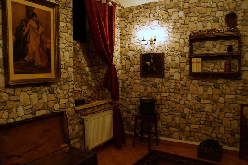 Dimly lit stone-walled room decorated with antique props, red curtains, and puzzle elements inside the Mind Maze escape room game in Prague, Czech Republic