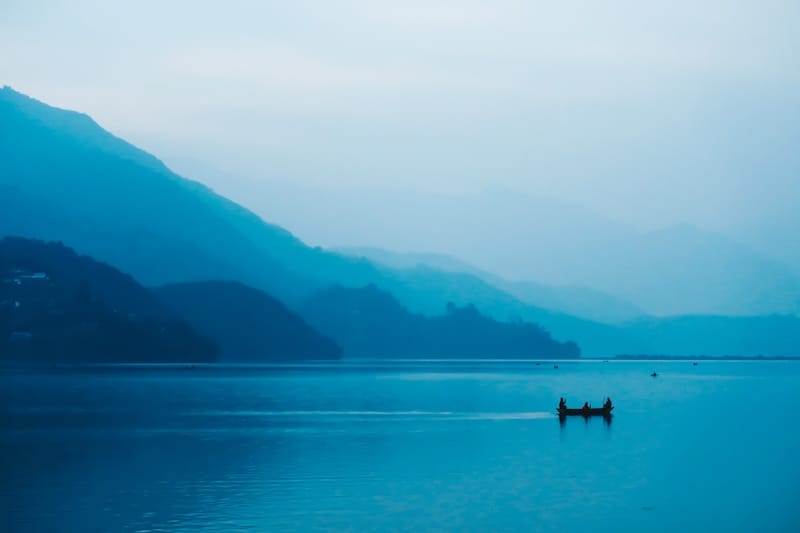 Moody muted blue colors over the lakeside views of a boat on the water in Pokhara, Nepal 
