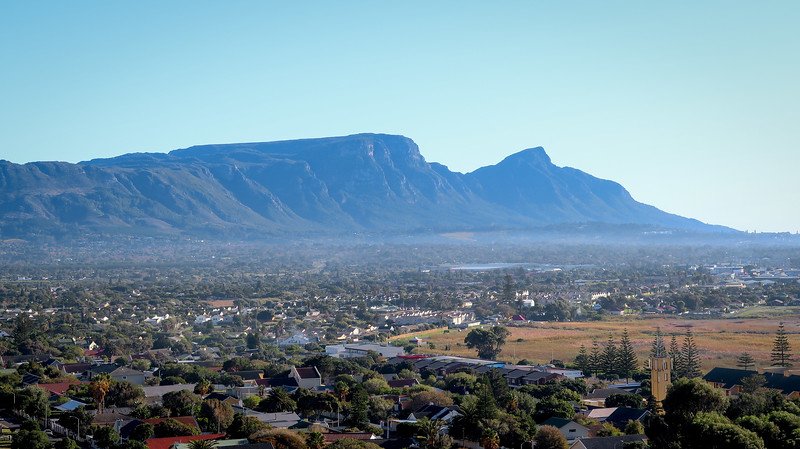 Panoramic view of Muizenberg, the first stop on our Cape Peninsula Sidecar Tour from Cape Town to the Cape of Good Hope. The photo captures the town’s rooftops with the dramatic silhouette of the surrounding mountains under a clear blue sky