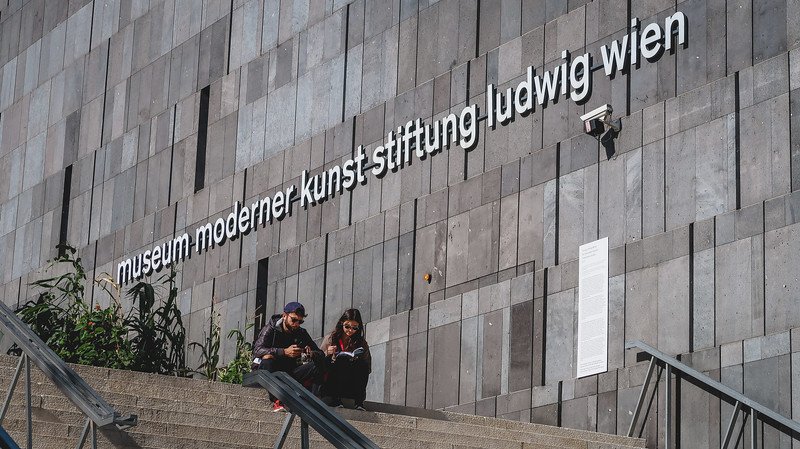 Visitors sitting on the steps outside the sleek grey façade of the Museum Moderner Kunst Stiftung Ludwig Wien (MUMOK) in the MuseumsQuartier of Vienna, Austria Visitors sitting on the steps outside the sleek grey façade of the Museum Moderner Kunst Stiftung Ludwig Wien (MUMOK) in the MuseumsQuartier of Vienna, Austria