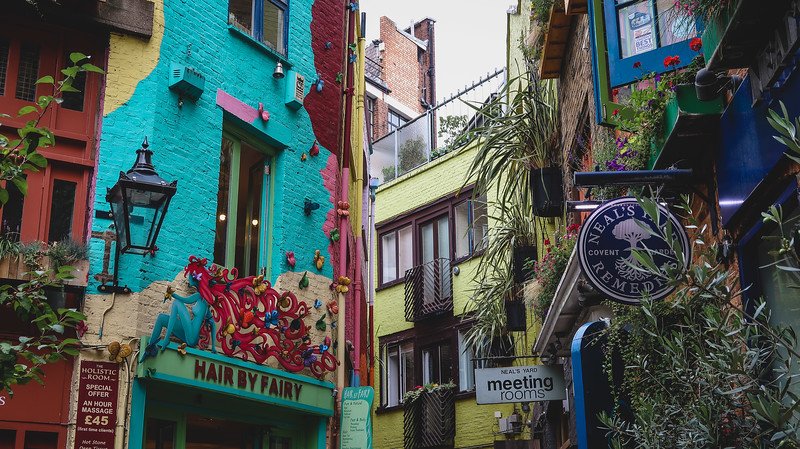 Vibrant facades of Neal’s Yard in London’s Seven Dials, with bright turquoise, red, and yellow buildings decorated with plants, shop signs, and quirky details, showcasing the lively and artistic atmosphere of this hidden urban courtyard