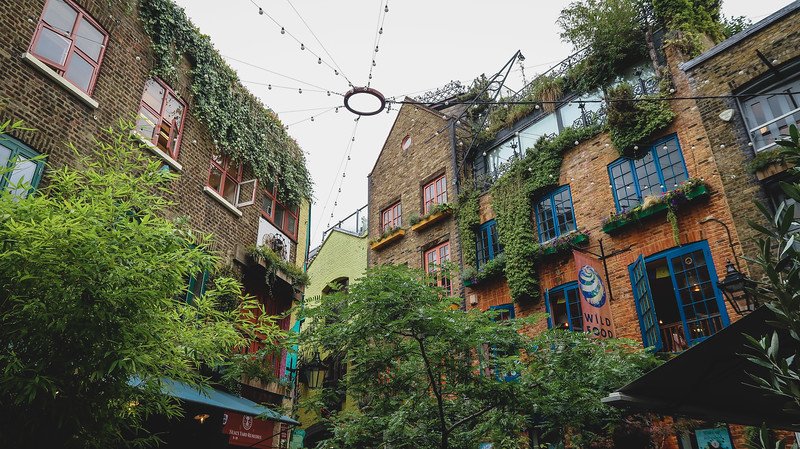 Colorful buildings covered in greenery surround Neal’s Yard in London’s Seven Dials, with bright windows, open shutters, and hanging string lights above, creating a hidden courtyard atmosphere that embodies the city’s bohemian charm