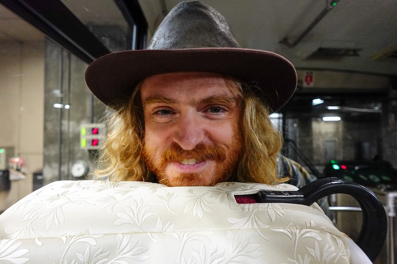 Nomadic Samuel all smiles wearing a hat on the bus journey during Tateyama Kurobe Alpine Crossing in Japan 