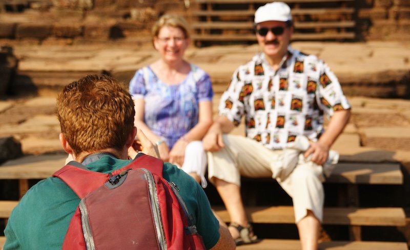Nomadic Samuel photographing tourists at Angkor Wat temple complex in Cambodia, capturing travel memories