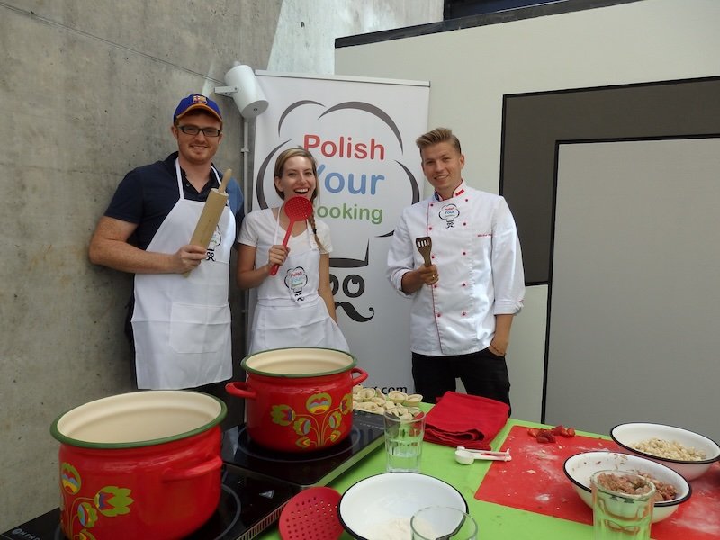 Nomadic Samuel and Audrey Bergner of That Backpacker smiling with a Polish chef at Polish Your Cooking in Warsaw, proudly holding utensils after making traditional pierogi during a hands-on cooking class that showcases authentic Polish food culture