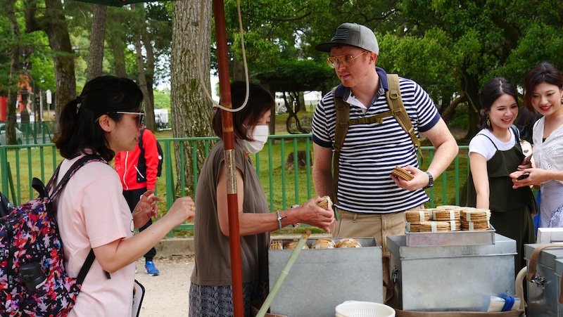 Nomadic Samuel buying deer crackers snacks to feed the deers in Nara, Japan from a lady selling them Nomadic Samuel buying deer crackers snacks to feed the deers in Nara, Japan from a lady selling them